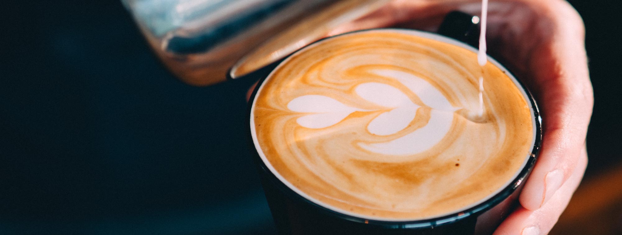 Person pouring a drink into a cup with latte art on a dark background