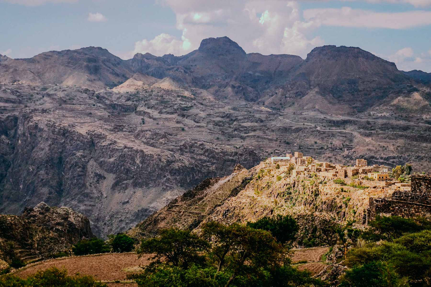 Walled village nestled in a mountainous landscape of Yemen with a clear sky.
